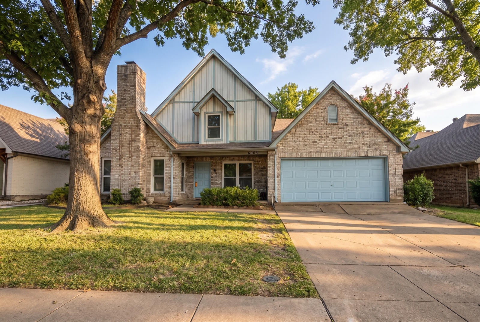 Two-story brick single-family home with a light-blue double garage door in Arlington, Texas at golden hour