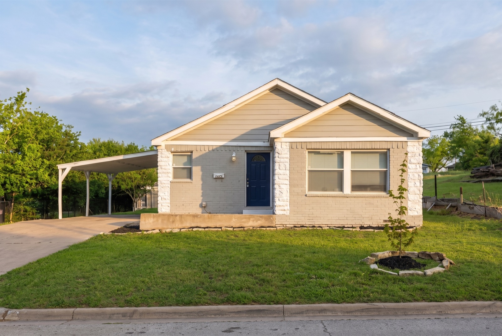 Single-story cottage with whitewashed stone walls, navy front door, and white carport in southeast Fort Worth, Texas